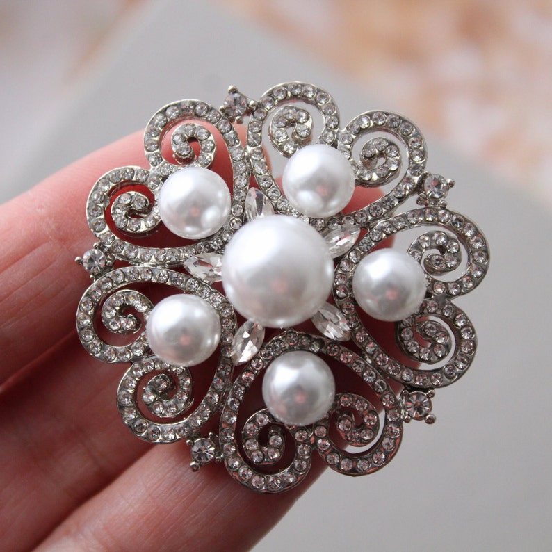 May include: A silver brooch with a floral design and multiple pearl accents.