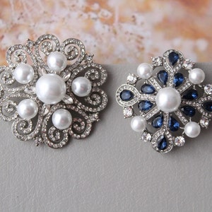 May include: Two silver brooches with pearl and crystal accents. One brooch features a floral design with white pearls, while the other has a snowflake design with blue crystals.