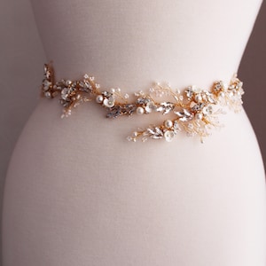 May include: A gold bridal belt featuring delicate floral and leaf designs, embellished with white pearls and clear rhinestones.