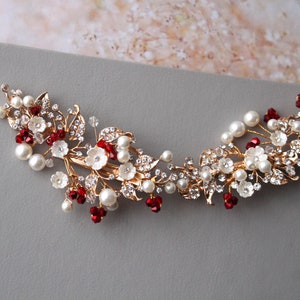 May include: Gold hair comb featuring white flowers, red crystals, and pearls. The comb is designed in a floral pattern with leaves and branches.