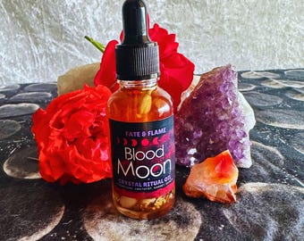 Może przedstawiać: Mała szklana butelka z olejkiem rytualnym Blood Moon Crystal Ritual Oil z czarną etykietą i złotymi napisami. Etykieta zawiera napis "Fate & Flame" i przedstawia sierp księżyca z czterema fazami. Butelka jest otoczona czerwonymi różami i kryształami.