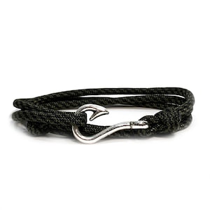 May include: A dark green and black rope bracelet with a silver-colored hook clasp. The bracelet is wrapped around itself, showcasing the texture of the rope and the shine of the metal clasp. The design is simple and rugged.