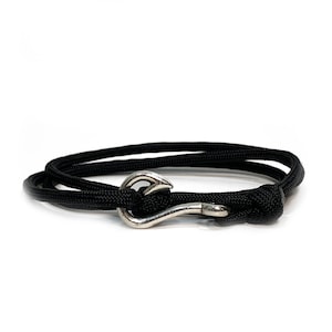 May include: A black rope bracelet with a silver-colored hook clasp. The bracelet is wrapped around itself, showcasing the hook closure. The design is simple and nautical, suitable for everyday wear.