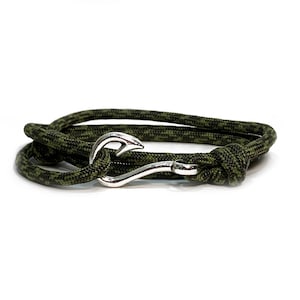 May include: A camouflage green and black rope bracelet with a silver-colored hook clasp. The bracelet is coiled on a white background, showcasing the texture of the rope and the metallic sheen of the clasp. The design is simple and rugged.