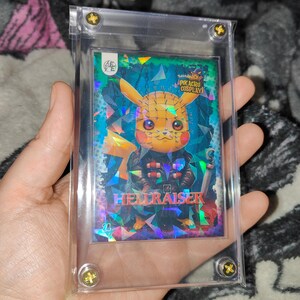 May include: A rectangular trading card encased in a clear magnetic acrylic holder with gold screws. The card features a holographic Pikachu character dressed as Pinhead, with the text Pikachu Cosplay and Hellraiser printed on the front.