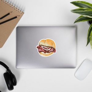 May include: A close-up of a small sandwich with a round bun, filled with thinly sliced meat and a white onion ring. The sandwich is on a white background.