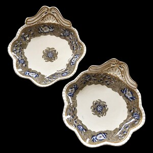 May include: Two decorative, scalloped-edge serving dishes. The dishes have a white center with a blue floral design and a gray border with blue flowers. The rims are trimmed with gold accents.