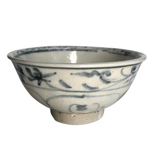 May include: A small, off-white ceramic bowl with a rounded shape and a short, circular base. The bowl is decorated with a blue floral pattern around the exterior. The rim is slightly flared.