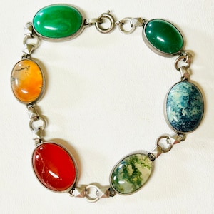May include: Silver-toned bracelet featuring seven oval-shaped gemstones in various colors: green, orange, red, and blue. The gemstones are set in individual bezels and connected by a series of small, geometric links. The bracelet has a clasp closure.