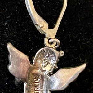 May include: A sterling silver angel earring with a lever back closure. The angel has detailed wings and the word "STERLING" is stamped on the body. The earring is shown against a dark background.