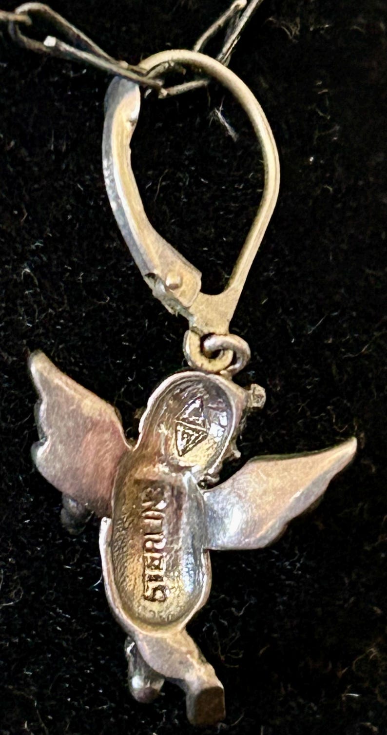 May include: A sterling silver angel earring with a lever back closure. The angel has detailed wings and the word "STERLING" is stamped on the body. The earring is shown against a dark background.