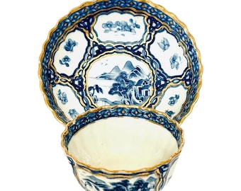 May include: A porcelain teacup and saucer set featuring a white base with intricate blue landscape illustrations, floral motifs, and a scalloped rim accented with gold trim. The design includes a central mountain scene on the saucer.