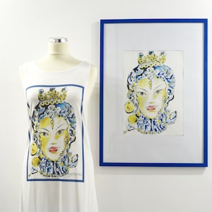 May include: White sleeveless dress with a blue and yellow print of a woman's face. The dress has a high-low hemline with blue tassels. A framed print of the same image is hanging on the wall behind the dress.