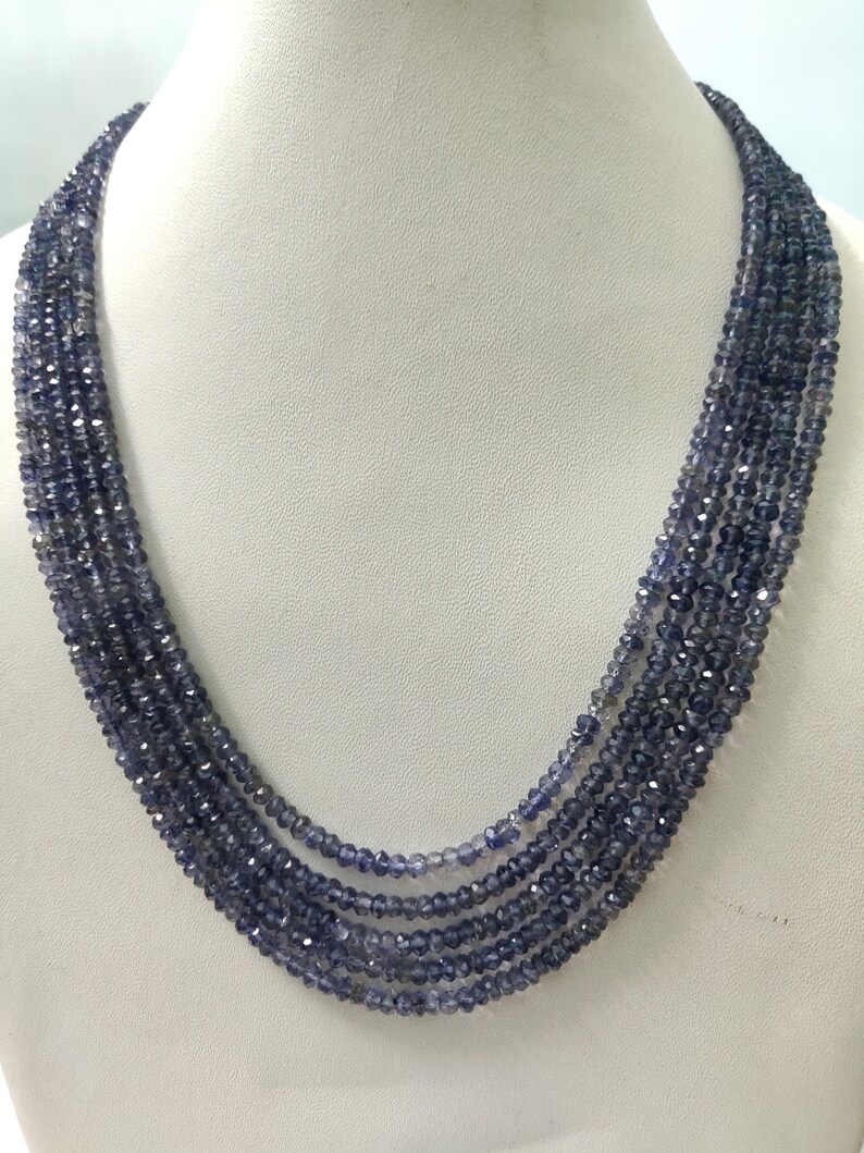 K&ouml;nnte beinhalten: Eine mehrstr&auml;ngige Halskette aus kleinen, facettierten, dunkelblauen Perlen. Die Halskette ist auf einer wei&szlig;en Mannequin-B&uuml;ste drapiert, die ihr mehrschichtiges Design und die subtilen Farbvariationen der Perlen hervorhebt.