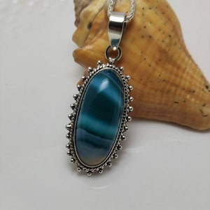 May include: A silver pendant necklace with a blue and white agate stone set in a silver oval frame. The pendant is on a silver chain.