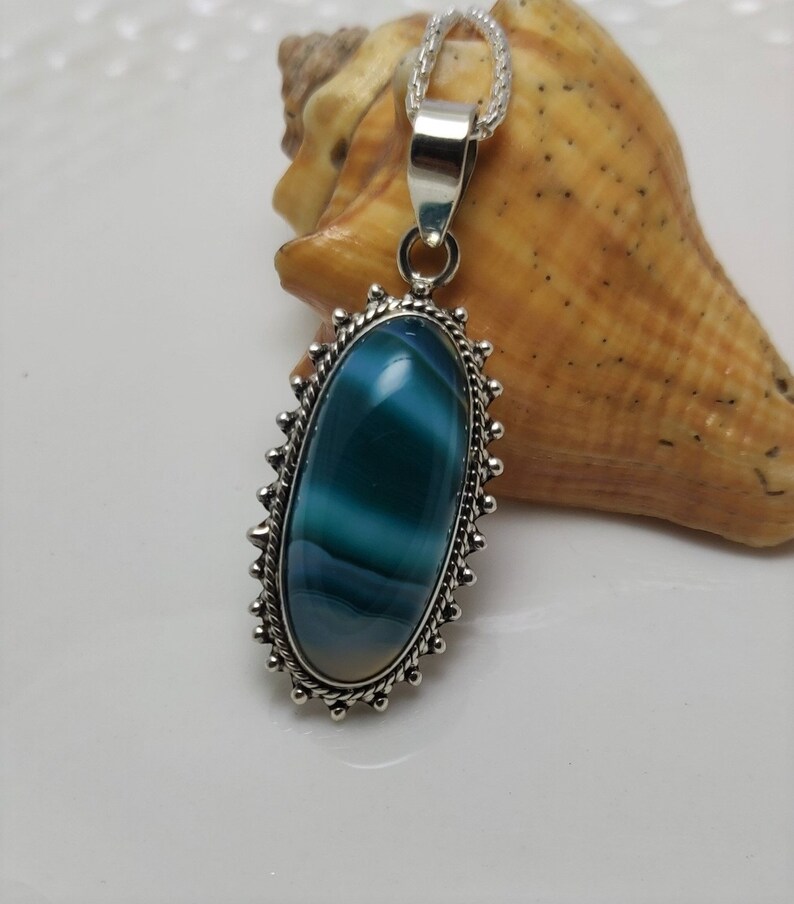 May include: A silver pendant necklace with a blue and white agate stone set in a silver oval frame. The pendant is on a silver chain.