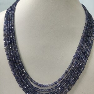 K&ouml;nnte beinhalten: Eine mehrstr&auml;ngige Halskette aus kleinen, facettierten, blau-violetten Perlen. Die Halskette ist auf einer wei&szlig;en Mannequin-B&uuml;ste drapiert, die ihr mehrschichtiges Design und ihre Farbe hervorhebt. Die Perlen haben einen subtilen Glanz.