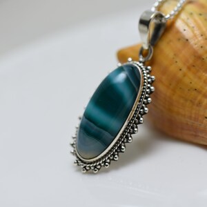 May include: A silver pendant with a green and white agate stone set in a beaded border.