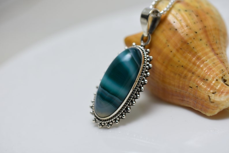 May include: A silver pendant with a green and white agate stone set in a beaded border.