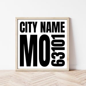 May include: A square wall art print in a light wood frame featuring bold black text on a white background. The text reads CITY NAME, followed by the large letters MO and the vertical number 63101. The design is centered within the frame.
