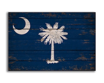 May include: A distressed wooden sign with the South Carolina state flag painted on it. The flag features a white crescent moon and palmetto tree on a blue background.