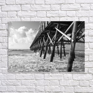 Pu&ograve; includere: Una fotografia in bianco e nero di un molo di legno che si estende su un mare mosso. Il molo &egrave; fatto di legno invecchiato e ha molti supporti. Il mare &egrave; agitato e ha onde.