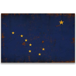 May include: A rectangular sign featuring the flag of Alaska. The flag has a dark blue background with eight gold stars. The stars are arranged in the shape of the Big Dipper and the North Star. The edges have a distressed, rusty appearance.