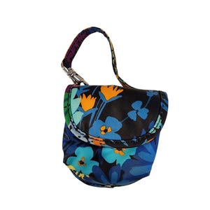 May include: A small, rounded pouch with a flap closure, featuring a vibrant floral pattern in shades of blue, turquoise, and orange against a black background. It includes a fabric handle attached with a silver-toned metal lobster clasp.