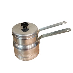 May include: A vintage aluminum stovetop espresso maker with a lid and two handles. The lid has a black knob. The espresso maker is silver and shows signs of wear. It is designed for brewing coffee on a stovetop.