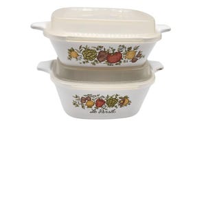 May include: Two off-white, rectangular casserole dishes with clear lids. Each dish features a colorful floral and vegetable design, including lemons, tomatoes, and artichokes. The text "Le Persil" is printed on the bottom dish.