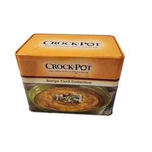 May include: A rectangular metal tin for a Crock-Pot recipe card collection. The lid and upper section are orange with the black text Crock-Pot The Original Slow Cooker. The lower section features a photograph of a bowl of soup with seeds.