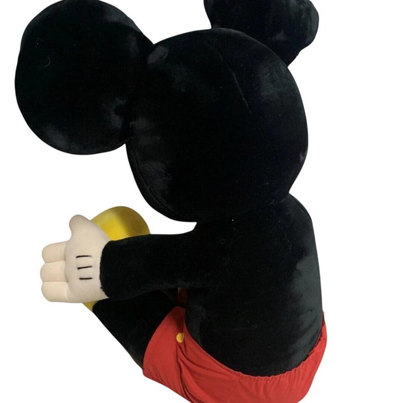 May include: A plush Mickey Mouse toy, featuring a black body, large ears, white gloves, and red shorts. The toy is in a seated position, with its arms outstretched. The plush toy is a classic Disney character.