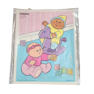 May include: A Playskool jigsaw puzzle in a plastic bag. The puzzle features two Cabbage Patch Kids, one riding a purple rocking horse and the other playing with alphabet blocks. The puzzle is in pastel colors and includes the text "Playskool".