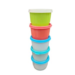 May include: A stack of four plastic containers with lids. The top container is lime green, the second is pink, the third is white, and the bottom is white with a blue lid.