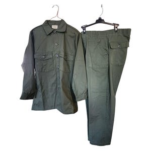 May include: Olive green military-style shirt and pants set. The long-sleeved shirt has two chest pockets and button closures. The pants have two front pockets and two back pockets. The set is hanging on separate hangers against a white background.