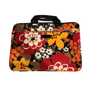 May include: A floral laptop bag with a black handle and zipper. The bag features a vibrant pattern of large red, yellow, and white flowers with orange accents on a black background. The brand name "VERA BRADLEY" is visible.