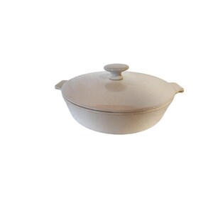 May include: A light-colored, oval-shaped Dutch oven with a matching lid. The lid has a small, rounded handle. The oven has two small handles on either side. The cookware is made of cast iron.