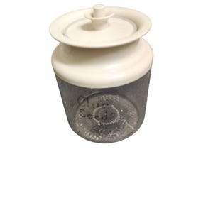 May include: A white plastic jar with a clear glass bottom. The jar has a white lid with a small knob on top. The jar is labeled "Chia Seeds".