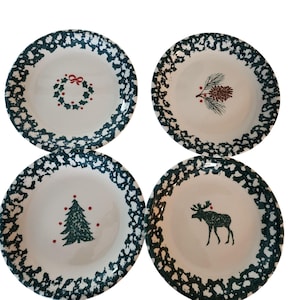 May include: Set of four green and white ceramic dinner plates with a Christmas theme. Each plate features a different design: a wreath, a pine cone, a Christmas tree, and a moose.