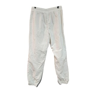 May include: Off-white athletic pants hanging against a white background. The pants have an elastic waistband and cuffs, with a drawstring. The material appears to be lightweight and slightly wrinkled.