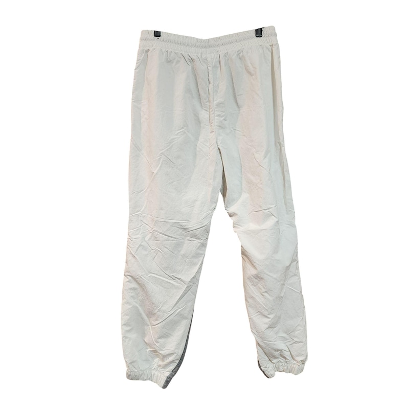 May include: Off-white athletic pants hanging against a white background. The pants have an elastic waistband and cuffs, with a drawstring. The material appears to be lightweight and slightly wrinkled.