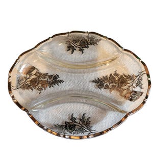 May include: A clear glass divided serving dish with a silver rim and floral design. The dish has three sections and a scalloped edge. The floral design is in silver and gold tones.