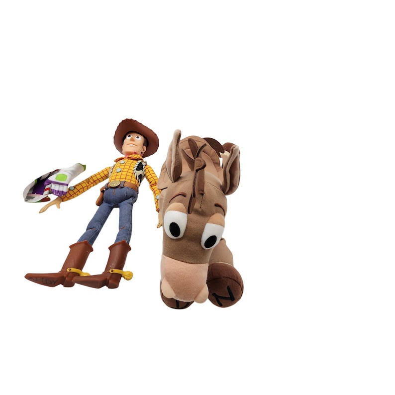 May include: A plush Woody doll in a cowboy hat, yellow plaid shirt, blue jeans, and brown boots, holding a Buzz Lightyear toy. Beside it is a plush brown horse head with large, expressive eyes. Toy Story themed.