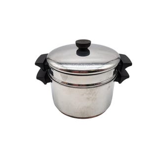 May include: A stainless steel steamer pot with a lid and black handles. The pot has a two-tiered design, with a lid featuring a black knob. The pot is designed for cooking food using steam.