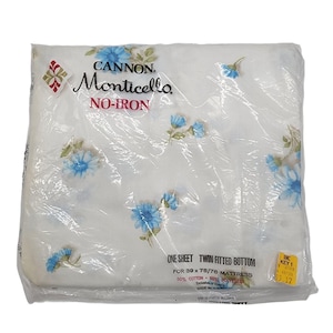 May include: A packaged twin fitted bottom sheet with a floral pattern. The sheet is white with blue flower designs. The packaging reads "CANNON Monticello NO-IRON" and is designed for a 39 x 75/76 inch mattress.