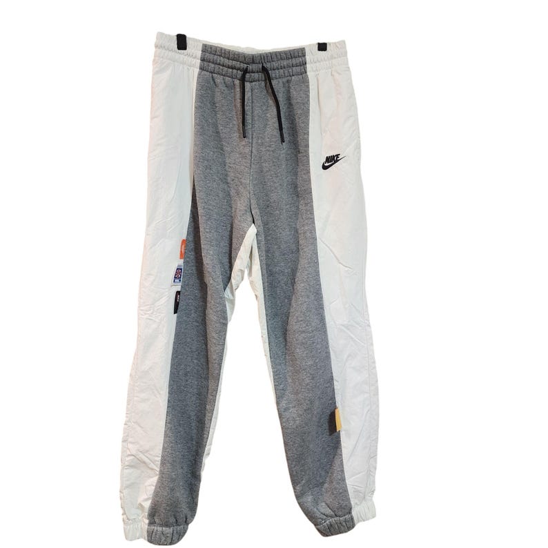 May include: Gray, white, and black Nike sweatpants. The sweatpants have a drawstring waist and a small Nike logo on the front. The pants are divided into three vertical sections of gray and white. There are small patches on the side.