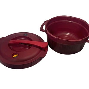 May include: A burgundy-colored pressure cooker with a matching lid and a separate bowl. The lid has a red handle and a pressure release valve. The bowl has two handles.