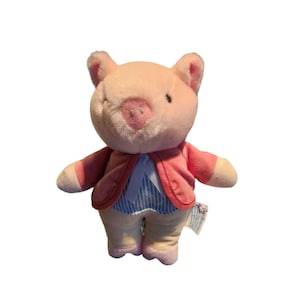 May include: A plush pig toy with a pink body, ears, and snout. It wears a red jacket over a blue and white striped shirt and tan pants. The pig has a friendly expression and is standing upright.