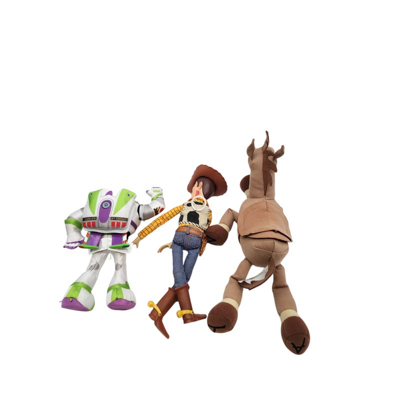May include: Three plush toys from the Toy Story franchise. Buzz Lightyear in a white and green spacesuit, Woody in a cowboy outfit, and a brown horse. The toys are set against a white background.