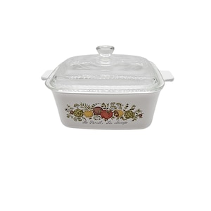 May include: White casserole dish with a clear glass lid. The dish features a colorful floral and vegetable design with the text "Le Persil, La Sauge". The lid has a clear knob handle and the dish has white handles on each side.